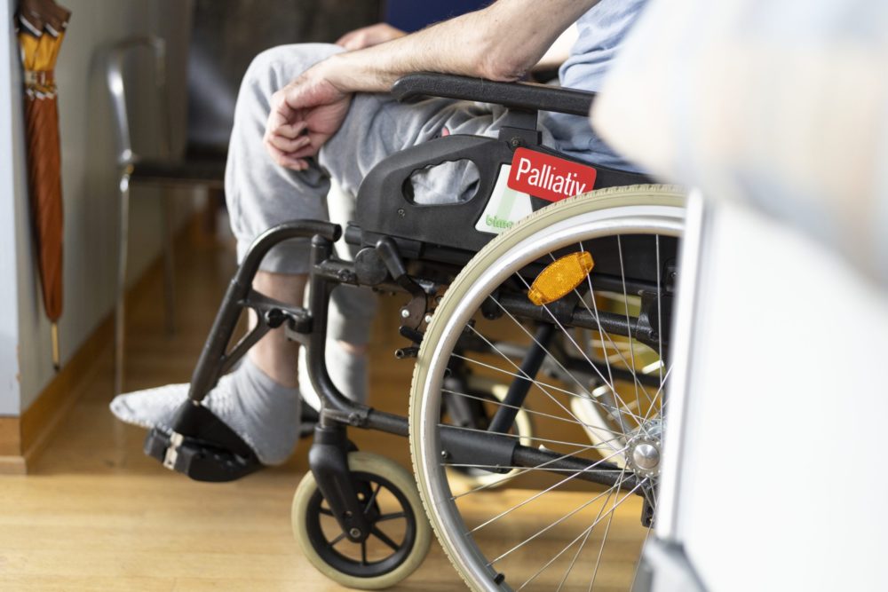 Ein Mann sitzt in einem Rollstuhl, der mit Palliative Care beschriftet ist.